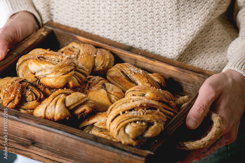 Woman in beige knitted sweater hold in hands wooden tray with home made traditional Swedish cardamom or cinnamon sweet buns Kanelbulle photo