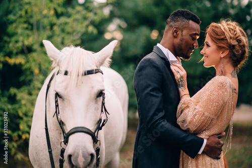Newlyweds are standing near a white horse in nature