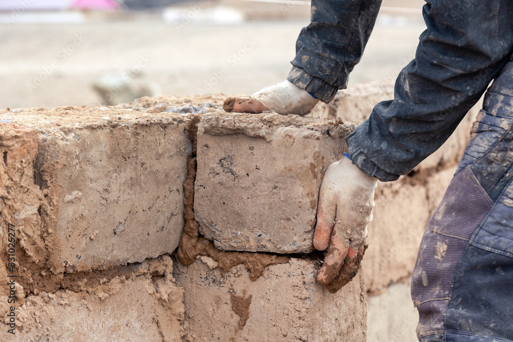 Close-up male hands build wall of unfinished house from clay brick Close-up male hands build wall of unfinished house from clay brick