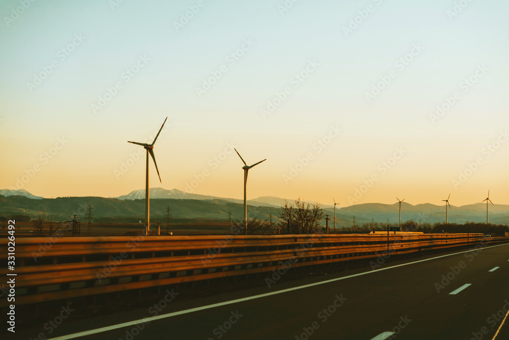 Photo of Eolian energy, Go green, Wind turbines along the road at sunset