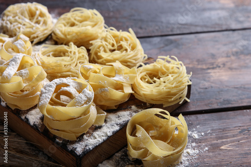 Concept of Italian cuisine. Dry pasta fettuccine and capellini with bowl with flour  eggs and wheat ears on an old wooden background. Background image  copy space