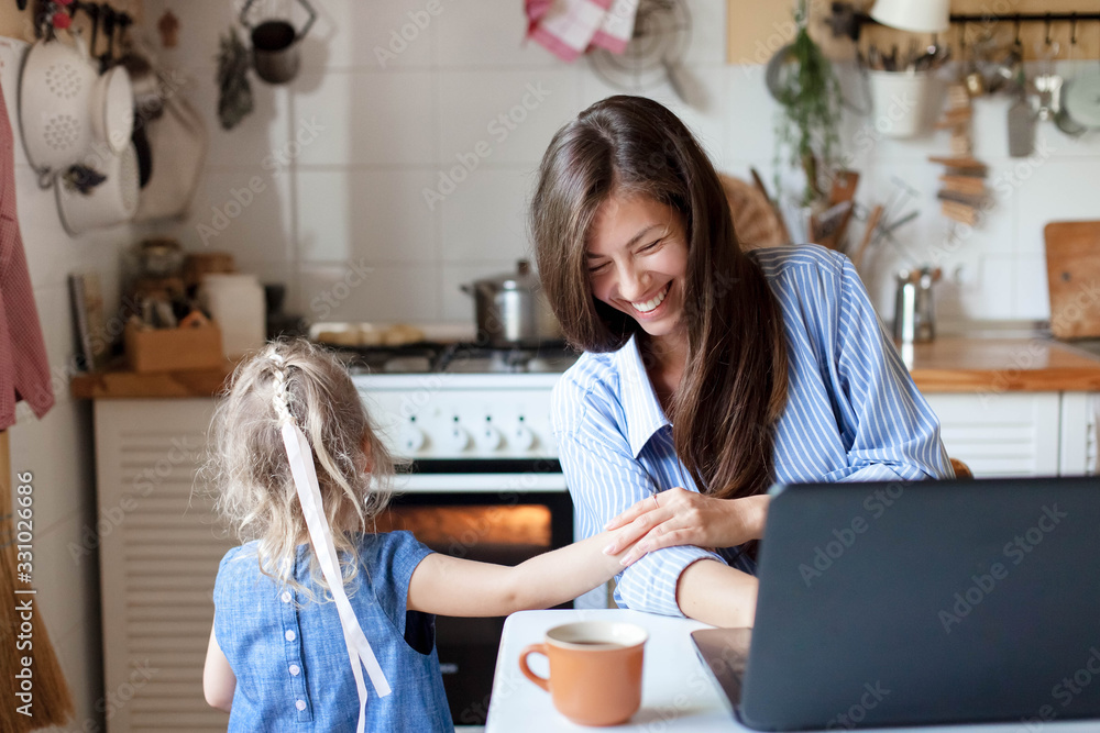 Working mom works from home with kid. Happy mother and daughter have fun. Successful woman and cute child using laptop. Freelancer workplace in kitchen. Female business. Lifestyle authentic moment - obrazy, fototapety, plakaty 