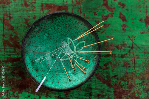 green ceramic Asian Bowl with needles for acupuncture on an old green paint wooden background photo