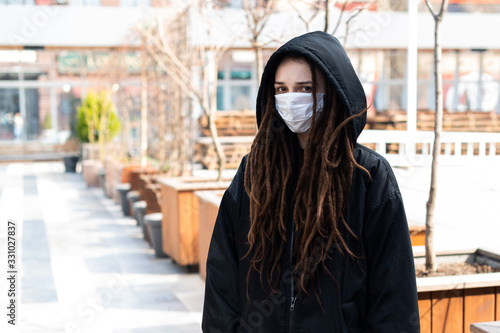 sad girl in a white medical mask and black hood on the street