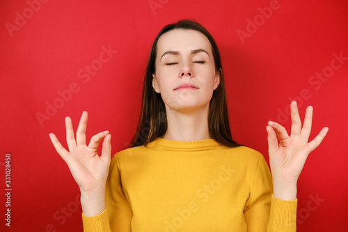 Beautiful attractive young woman in yellow sweater doing yoga exercise girl meditating standing over red background closed eyes feels internal balance make fingers mudra gesture, no stress concept
