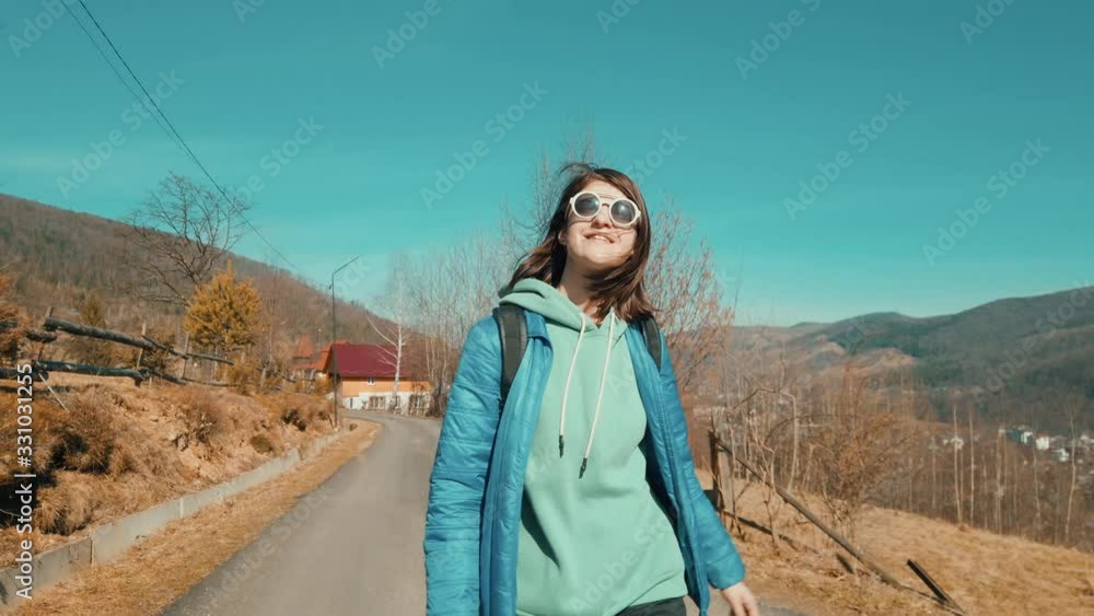 Female backpacker walking at the village road at the sunny day. Looking at the mountains in background. Girl traveler enjoying of outdoor traveling. Recreating of life and self isolating. Female backpacker walking at the village road at the sunny day. Looking at the mountains in background. Girl traveler enjoying of outdoor traveling. Recreating of life and self isolating.