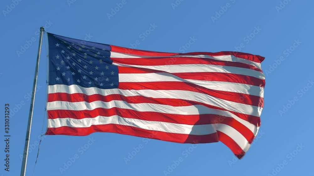American flag on a blue sky background. USA flag flaping in wind. Close-up of an American flag flying in the wind against a background of clear sky. Close up of American flag waving. American concept. American flag on a blue sky background. USA flag flaping in wind. Close-up of an American flag flying in the wind against a background of clear sky. Close up of American flag waving. American concept.