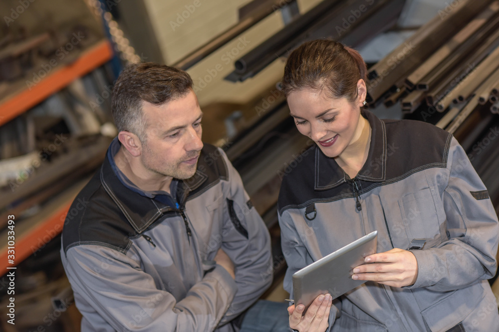 Confident female factory worker shows male colleague something o Confident female factory worker shows male colleague something o