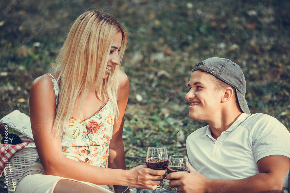 Beautiful smiling couple on the park making a picnic and drinking wine Beautiful smiling couple on the park making a picnic and drinking wine