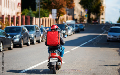 Deliveryboy on scooter with red backpack driving fast to customers, online orders. Courier delivering food on motorbike. Food supplier driving fast on motorcycle. Quick deliver food to customers