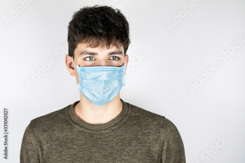 Guy with surgical medical mask on face on light background. The guy has a serious frightened face because he understands that a pandemic is dangerous © Мар'ян Філь