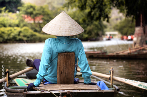 A vietnamese woman photographed from behind rowing with her feed with a vietnames hat