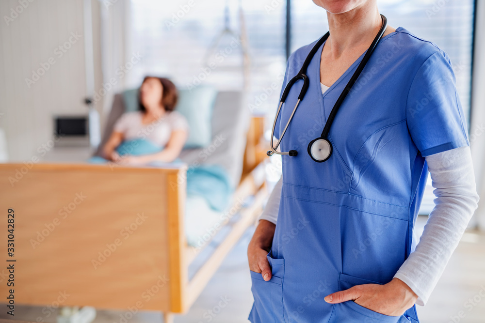 Unrecognizable doctor standing in hospital room, patient in the background. Unrecognizable doctor standing in hospital room, patient in the background.