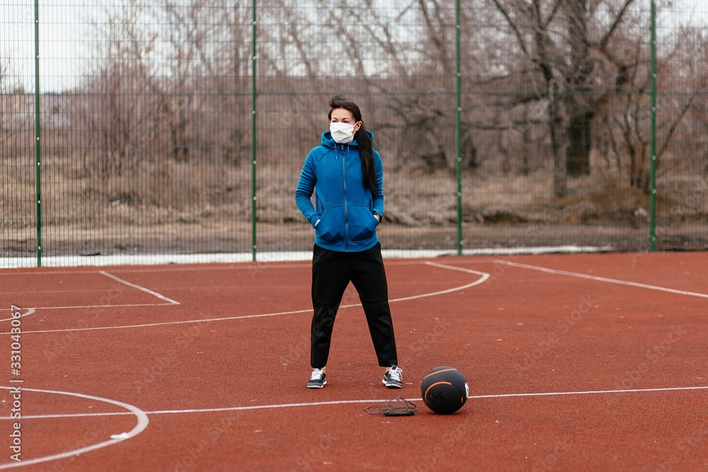 Obraz premium A young woman is playing sports on a sports field in a mask. Protection from coronavirus infection with a medical mask.