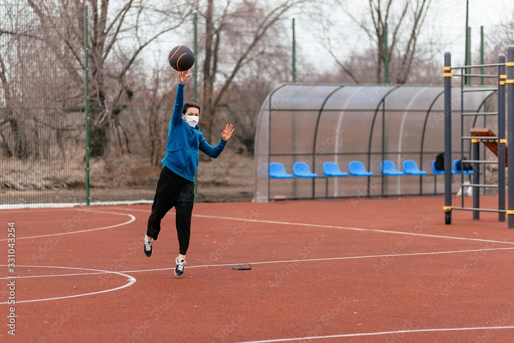 Obraz premium A young woman is playing sports on a sports field in a mask. Protection from coronavirus infection with a medical mask.