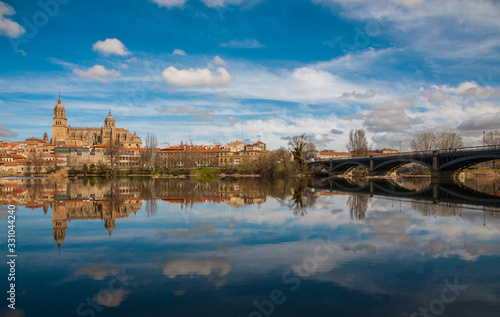 View of the Cathedral of Salamanca and the Enrique Estevan bridge reflected in the calm waters of the Tormes river