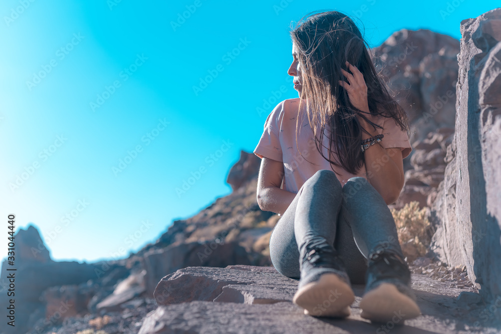 Naklejka premium Lifestyle, a young brunette sitting looking towards the horizon next to the Teide volcano. Tenerife