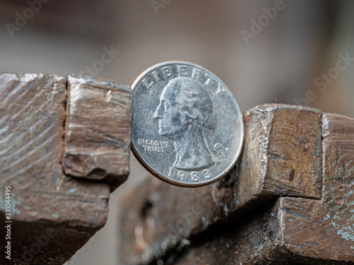 Quarter dollar coin clamped with a metal vise on both sides. Concept of financial and business problems. The economy is in the grip.
