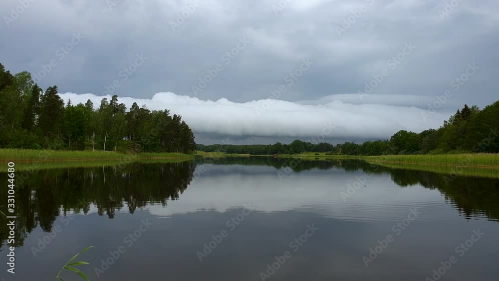 Gorgeous view of sunset on calm summer evening. Lake shore with green trees and plants reflecting in crystal clean mirror water surface. Sky covered with heavy thunder clouds. Slow motion. Gorgeous view of sunset on calm summer evening. Lake shore with green trees and plants reflecting in crystal clean mirror water surface. Sky covered with heavy thunder clouds. Slow motion.