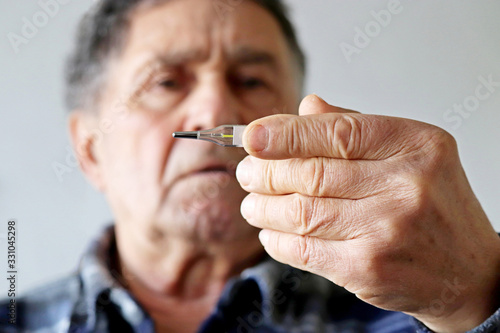 Elderly man measuring body temperature with mercury thermometer. Concept of fever, cold treatment, symptoms of coronavirus