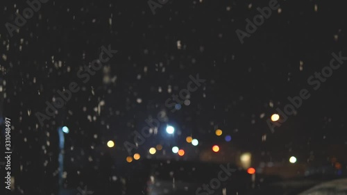 Snow flakes falling from the sky at night. Defocused street lights, snow falling in the dark at night.