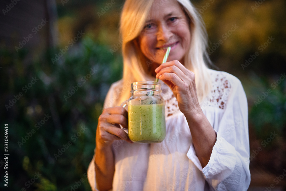 Senior woman with juice standing outdoors on terrace, looking at camera. Senior woman with juice standing outdoors on terrace, looking at camera.