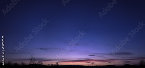 Beautiful blue, purple and orange twilight gradient sky during sunset in the early spring. Tree silhouettes, stitched panorama. 