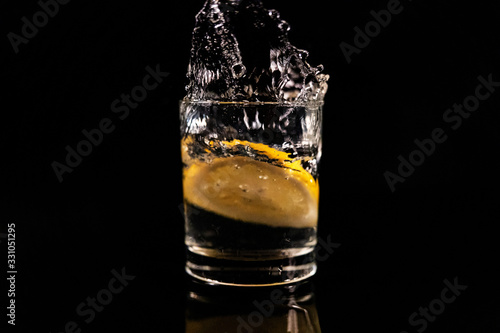 Splash in a glass with lemon on a black background. Fresh healthy drink concept