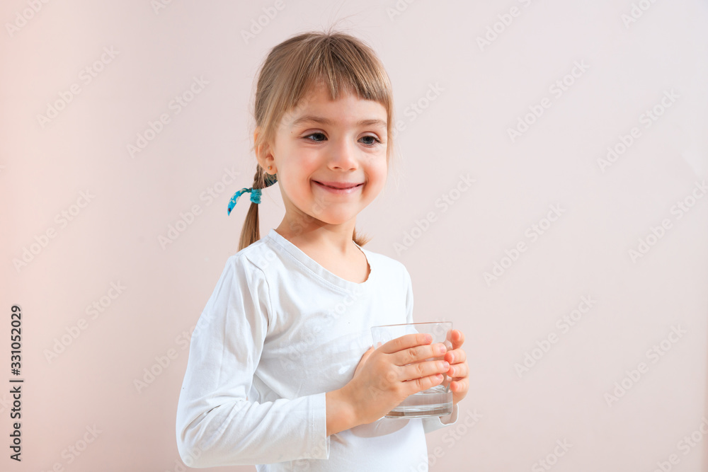 Cute smiling girl holding glass of water at neutral background. water balance concept. place for text Cute smiling girl holding glass of water at neutral background. water balance concept. place for text