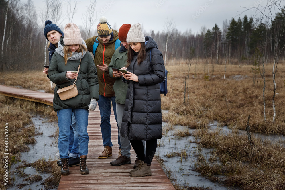Texting separately outdoors. A company of 5 friends each looks at his phone Texting separately outdoors. A company of 5 friends each looks at his phone