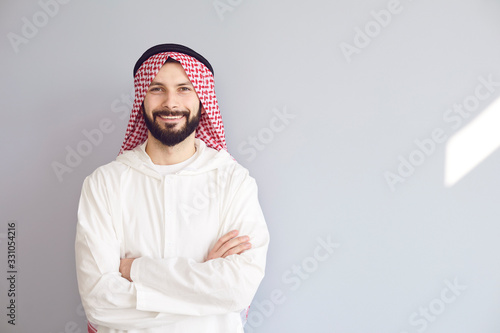 Foto Attractive smiling arab man crossed his arms on a gray background