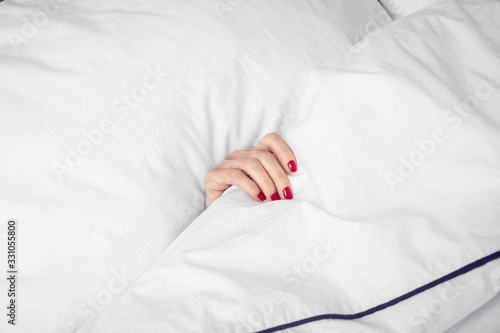 Hand mit roten lackierten Fingernägeln im Bett photo