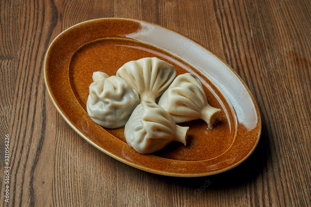 Appetizing homemade khinkali with different fillings (minced meat, cheese, vegetables or spinach) in a brown plate on a wooden background. Traditional Georgian cuisine. Georgian dumplings