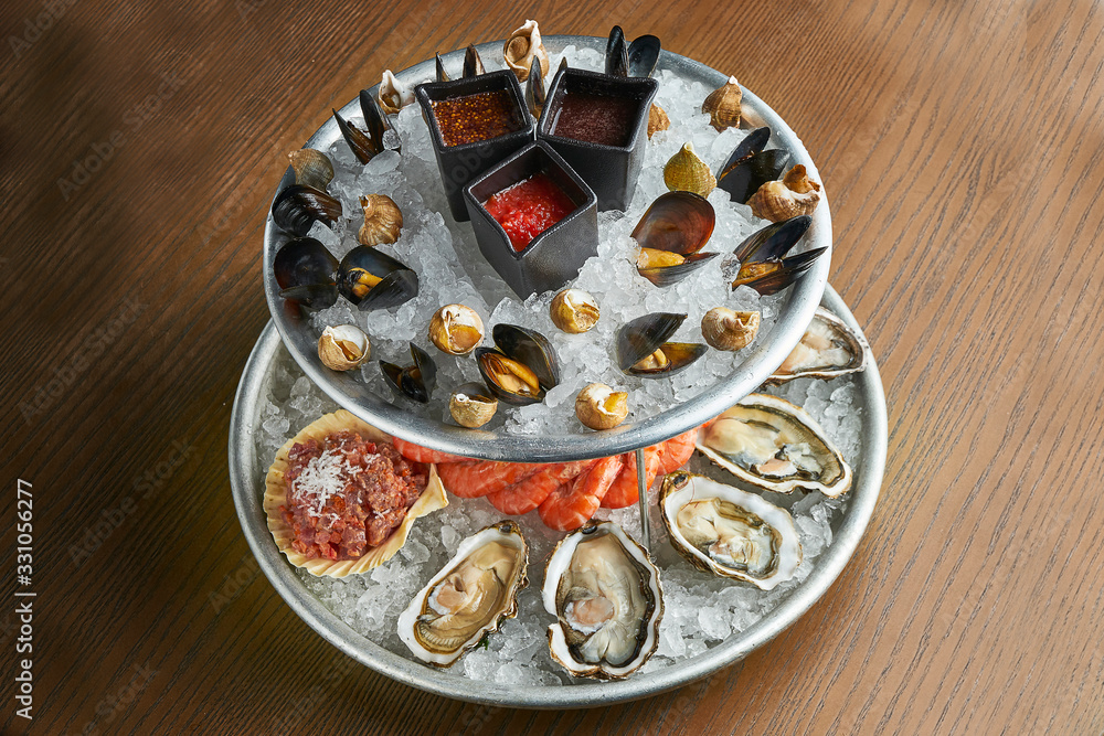 A large dish with fresh seafood on ice - oysters, shrimps, mussels, scallops. Close up. Catering A large dish with fresh seafood on ice - oysters, shrimps, mussels, scallops. Close up. Catering