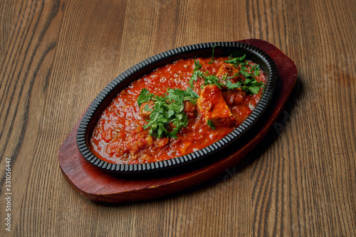 Close up view on traditional georgian cuisine Chakhokhbili - stewed chicken, tomato with fresh herbs on wooden background. photo