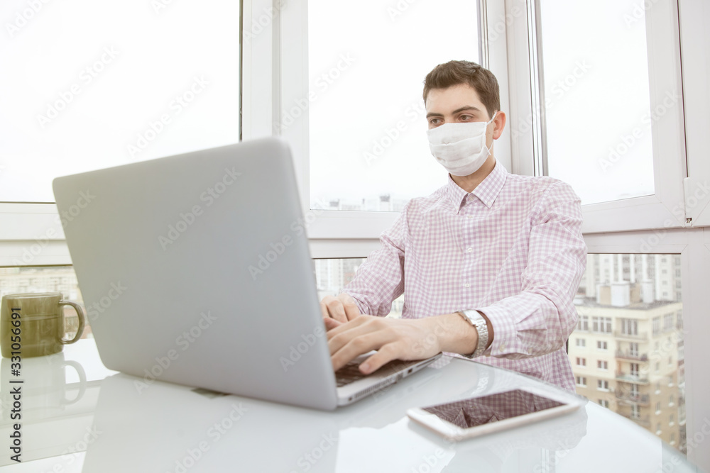 A guy in a protective face mask works at a computer from home during a virus epidemic. Quarantine during viral infection A guy in a protective face mask works at a computer from home during a virus epidemic. Quarantine during viral infection