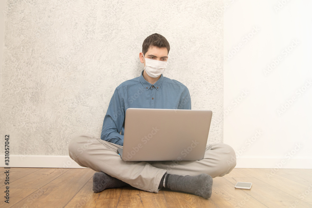 A guy in a protective face mask is working at a computer in an empty room at home during a virus epidemic. Quarantine during viral infection