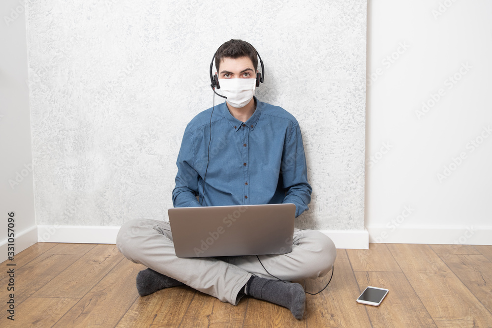 A guy in a protective face mask is working at a computer in an empty room at home during a virus epidemic. Quarantine during viral infection A guy in a protective face mask is working at a computer in an empty room at home during a virus epidemic. Quarantine during viral infection