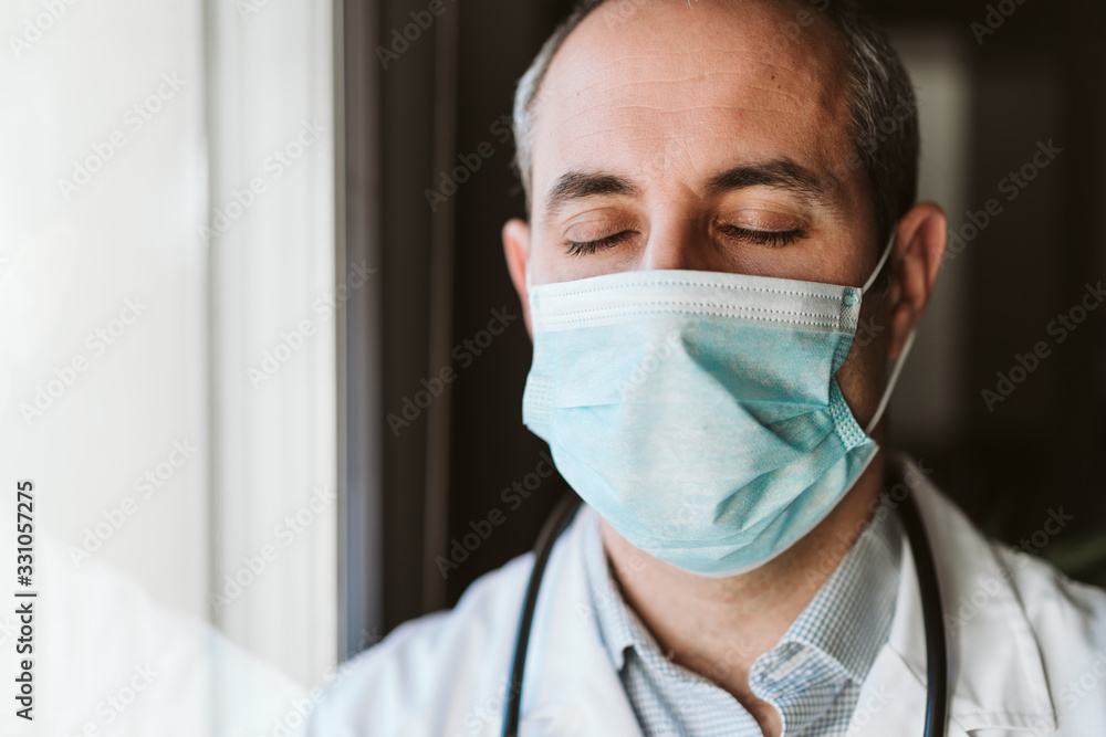 portrait of doctor man by the window wearing protective mask and gloves indoors. Corona virus concept portrait of doctor man by the window wearing protective mask and gloves indoors. Corona virus concept