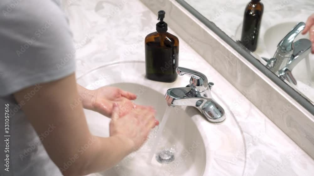 Over the shoulder shot of Woman washing her hands with soap and water to prevent spread of germs, bacteria, and viruses Over the shoulder shot of Woman washing her hands with soap and water to prevent spread of germs, bacteria, and viruses