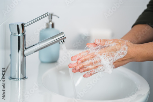Hygiene. Cleaning Hands. Washing hands with soap. Young woman washing hands with soap over sink in bathroom, closeup. Covid 19. Coronavirus. photo