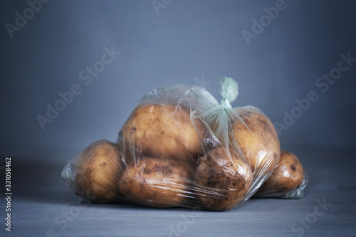 Recycling and environment idea: fresh potato in plastic package, wrapped in plastic cellophane on blue background