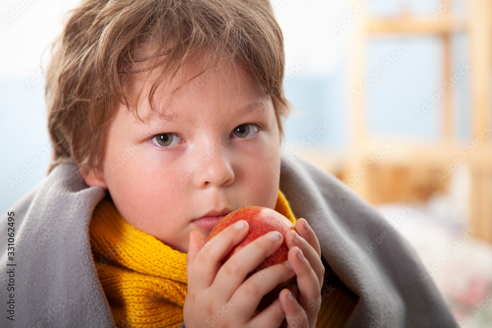 Sick boy in warm clothes holding fruit at home Sick boy in warm clothes holding fruit at home