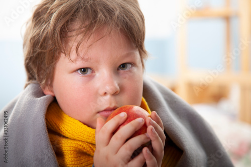 Sick boy in warm clothes holding fruit at home
