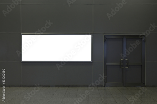 Billboard on a gray wall indoors next to a swing door.