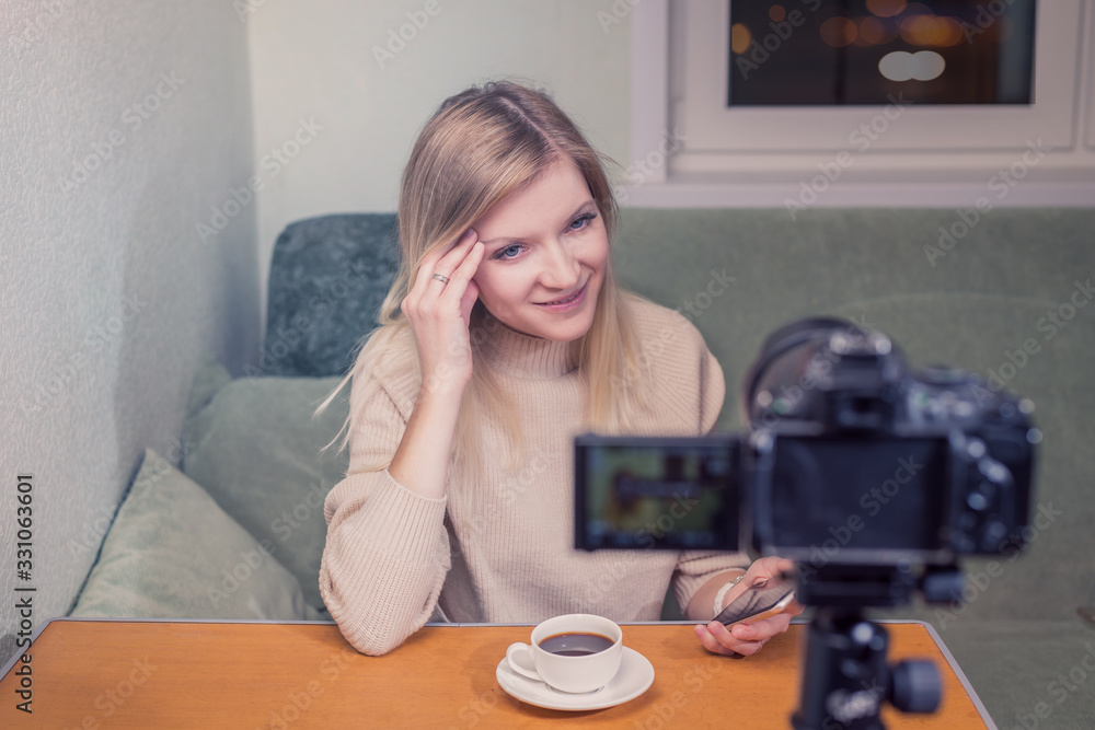 Woman blogger in front of camera recordind video. People, media and technology concept/Beautiful woman sitting at the table and looking in a front of camera, looks happy Woman blogger in front of camera recordind video. People, media and technology concept/Beautiful woman sitting at the table and looking in a front of camera, looks happy