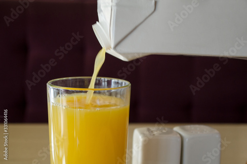 Yellow juice,  orange or mango,  or multifruit,  pours from a white packaging packing juice into a transparent glass