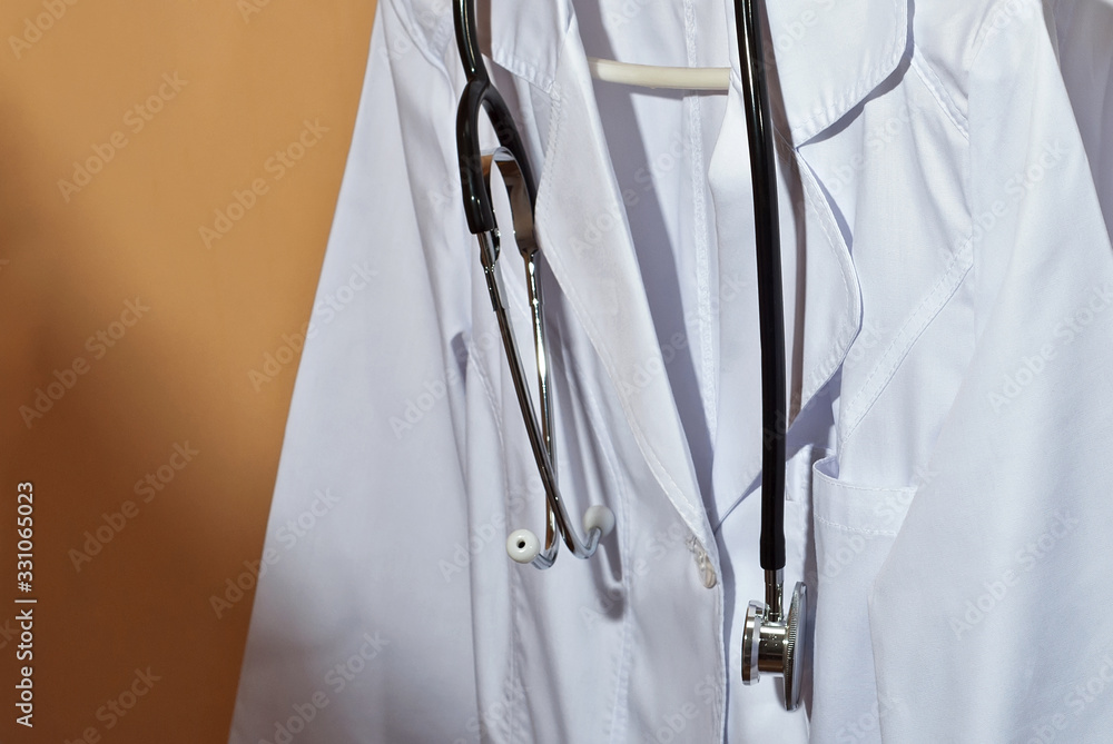 White medical gowns hang on hangers. Clothes with stethoscope on orange background. White medical gowns hang on hangers. Clothes with stethoscope on orange background.
