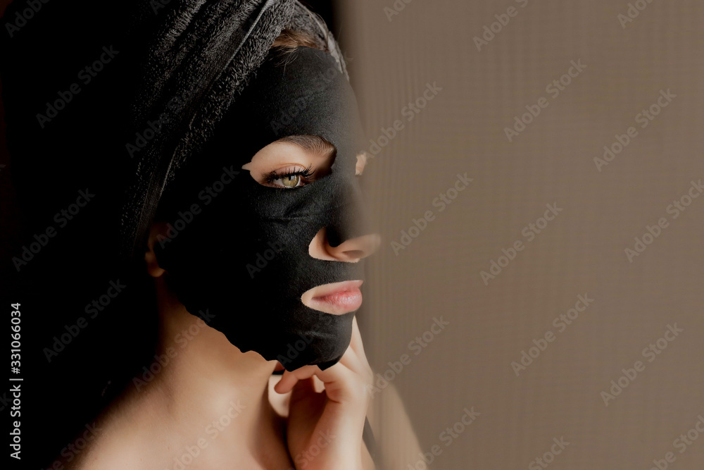 Beautiful Woman Applying Black Facial Mask. Beauty Treatments. Close-up Portrait of Spa Girl Apply Clay Facial mask on black background