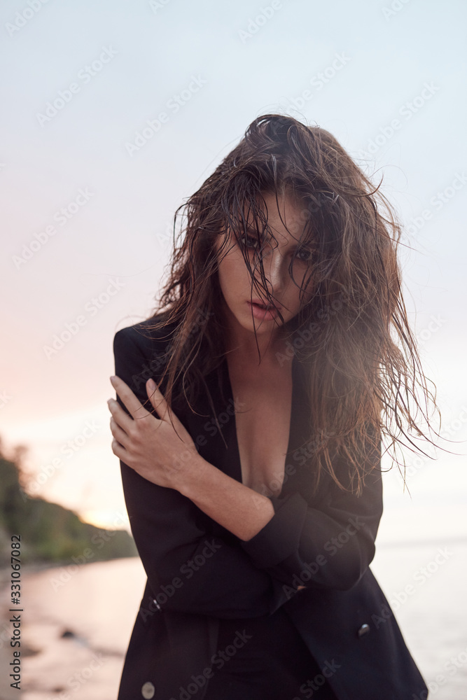 beautiful young and athletic girl on the beach dressed in a black suit, sea sunset, lifestyle and fashion